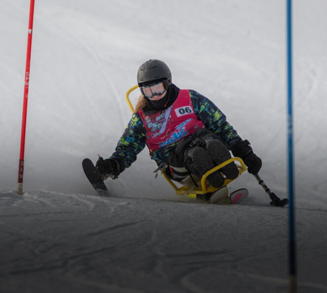 Para nordic athlete coming down a ski hill covered in snow. The athlete is weaying a black helmet with goggles, a red pinny